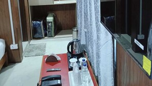 Une chambre de taille modeste, dotée d’une armoire en bois, d’un bureau avec un téléphone, d’une bouilloire et d’une bouteille d’eau.