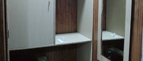 A small, enclosed bathroom with wooden paneling, a mirror, a toilet, and a trash bin.