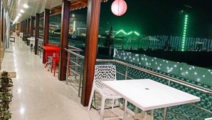 Un espace extérieur abrité, doté de tables et de chaises, d’une rambarde et offrant une vue sur le paysage urbain la nuit.