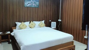 Une chambre avec un mur lambrissé en bois, un lit avec une literie blanche et quatre oreillers, une table de chevet avec une lampe et un téléviseur fixé au mur.