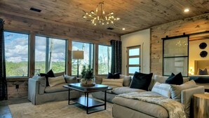 A cozy living room with a wooden ceiling, large windows, a sofa set, and a coffee table. - Casa Lotta | Hot Tub + Game Room + Fire Pit (Mineral Bluff)