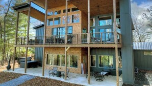 A multi-story wooden cabin with a balcony on the upper level, outdoor seating, and a large window overlooking the landscape. - Casa Lotta | Hot Tub + Game Room + Fire Pit (Mineral Bluff)