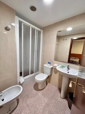 A bathroom with a toilet, bidet, sink, and a shower with frosted glass doors. - Pensión La Orozca (Benidorm)