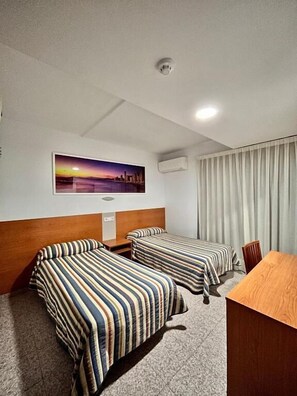A hotel room with two beds, a wooden desk, a painting of a sunset, an air conditioning unit, and a ceiling light. - Pensión La Orozca (Benidorm)