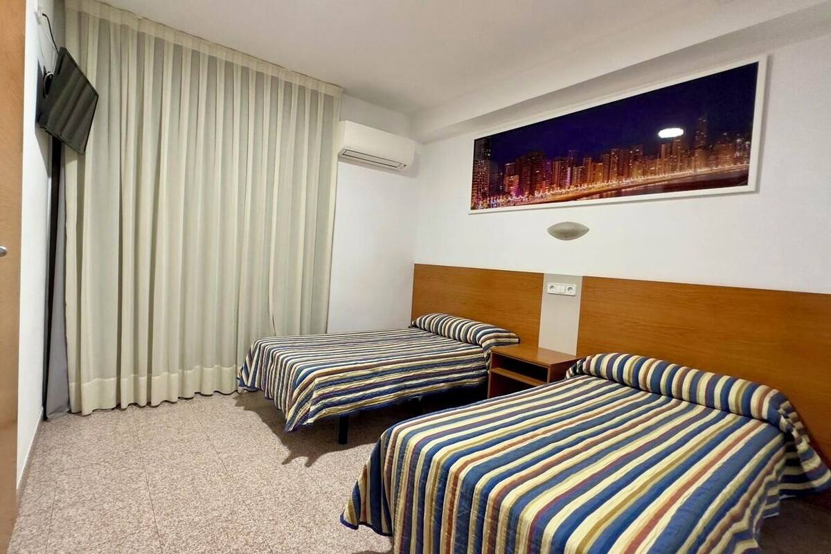 A hotel room with two beds, a cityscape view, a flat-screen TV, and an air conditioning unit.