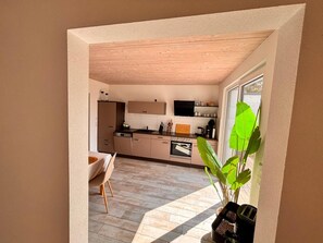 A modern kitchen with wooden cabinets, a dining area with a chair, and a large window with a plant. - Hegau apartment, 2.5 rooms, 70sqm, free WiFi and parking spaces (Tengen)