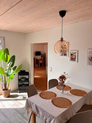 A dining area with a table set for two, a hanging pendant light, and a potted plant.