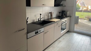 Cocina moderna con encimera negra, electrodomésticos de acero inoxidable y puerta corrediza de vidrio que da a un patio.