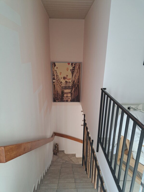 A staircase with a wooden handrail and black balusters, leading to a landing with a large framed artwork depicting a street scene.