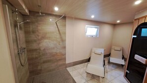Un baño moderno con ducha de vidrio, un ventanal pequeño y dos sillones reclinables.