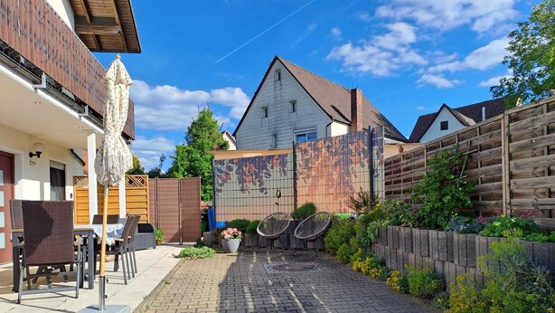Un patio empedrado con mesas al aire libre, una cerca de madera y un edificio con tejado inclinado.