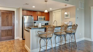 Una cocina con armarios de madera, un refrigerador de acero inoxidable, un microondas y una zona de bar con sillas de mimbre.