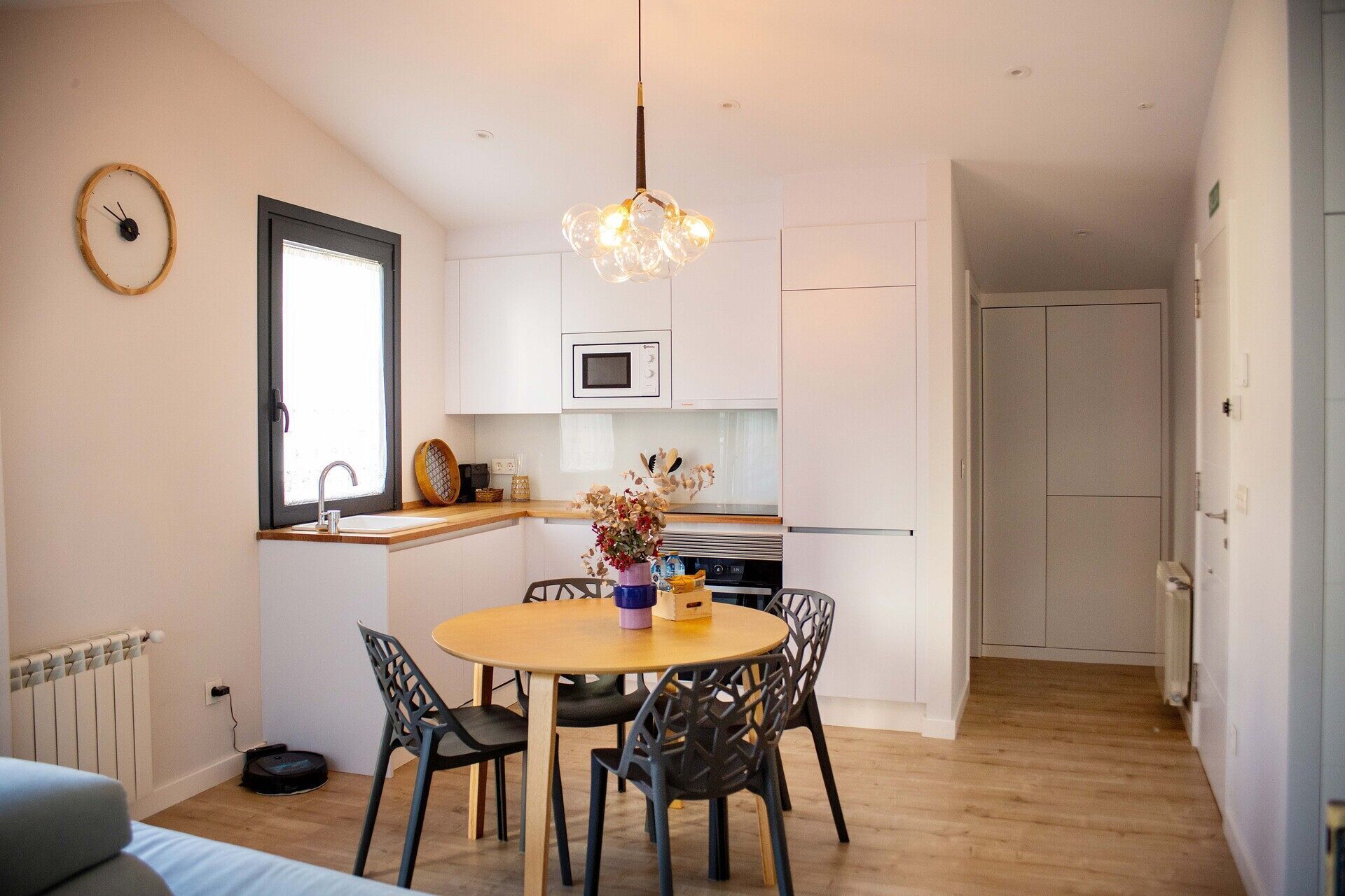 A compact kitchen with white cabinets, a microwave, and a dining area with a wooden table and chairs.