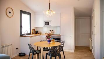 A compact kitchen with white cabinets, a microwave, and a dining area with a wooden table and chairs.