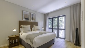 A bedroom with a large bed, bedside lamps, a window with curtains, and a standing heater. - Newly Renovated 3 bed Apartment With Splashpool - 2283 (Cape Town)