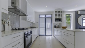 A modern kitchen with white cabinetry, a built-in oven, and a large window with blinds. - Newly Renovated 3 bed Apartment With Splashpool - 2283 (Cape Town)