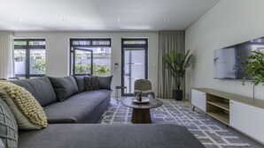 A modern living room with a grey sofa, a round coffee table, and a TV mounted on the wall. - Newly Renovated 3 bed Apartment With Splashpool - 2283 (Cape Town)
