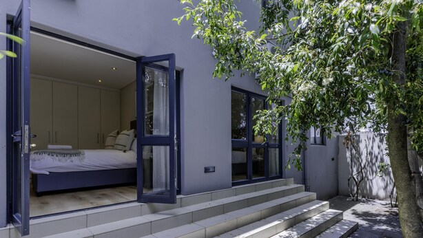 A modern bedroom with a bed, a large window, and a staircase leading to the entrance. - Newly Renovated 3 bed Apartment With Splashpool - 2283 (Cape Town)