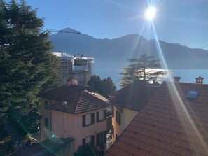 A coastal building with a tiled roof, a mountain in the background, and a clear sky. - Riflessi Sul Lago (Gravedona)