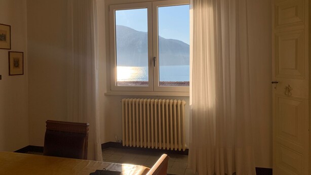 A room with a large window, a radiator, a wooden chair, and a bed. - Riflessi Sul Lago (Gravedona)