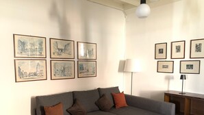 A living room with a grey sectional sofa, a wooden side table, and a lamp. There are six framed pictures on the wall. - Riflessi Sul Lago (Gravedona)