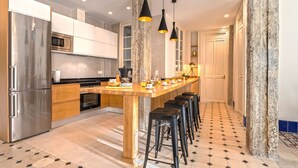Une cuisine moderne dotée d’un îlot central, d’appareils électroménagers en acier inoxydable et de tabourets de bar noirs.