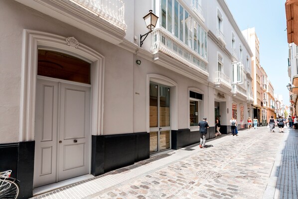 Un edificio histórico con fachada blanca, ventanas amplias y detalles de molduras negras en la base.