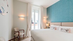 A hotel room with a large bed, a chair, a wall-mounted lamp, and a view through a window. - Genteel Home Sagasta (Cádiz)