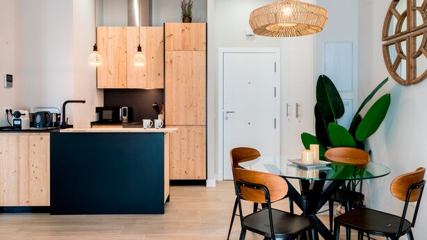 A modern kitchen with wooden cabinets, a central island, and a dining area with a glass table and chairs. - Genteel Home Sagasta (Cádiz)