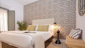 Quarto de hotel moderno com uma cama grande, mesa de cabeceira, abajur e um painel decorativo na parede.
