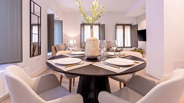 Uma sala de jantar moderna com uma mesa redonda, quatro cadeiras e um vaso com folhagem.