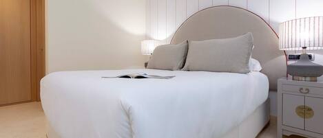 A neatly made bed with a white comforter and pillows, a bedside table with a lamp, and a wooden wardrobe in a hotel room.