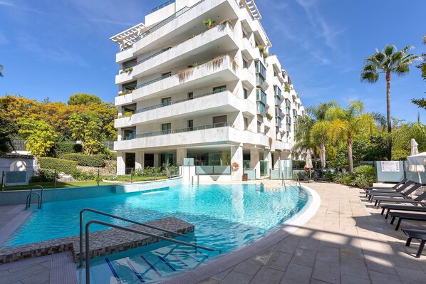 Un hotel a più piani con piscina, area salotto all'aperto e vegetazione rigogliosa.