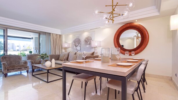 A dining area with a large round mirror, a chandelier, and a dining table set for six.