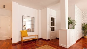 Un couloir avec un plancher en bois, un banc, un miroir, une porte et un meuble.