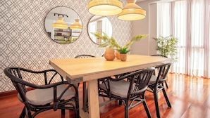 Un coin repas avec une table en bois, des chaises en osier noir et un mur orné d’un motif.