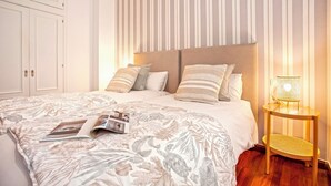 Une chambre à coucher bien rangée, avec un grand lit, des motifs rayés sur les murs et une table de chevet avec une lampe.