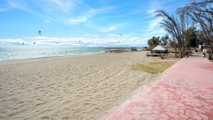 A beach with a paved walkway, a clear sky, and kites flying. - Genteel Home Guadalmansa Beach (Estepona)