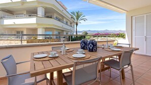 A wooden table set for dining with plates, cups, and a vase on an outdoor terrace with a view of a multi-story building and mountains in the background. - Genteel Home Guadalmansa Beach (Estepona)