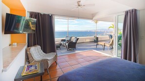 Ein Hotelzimmer mit Bett, Fernseher, einem Balkon mit Stühlen und Meerblick.
