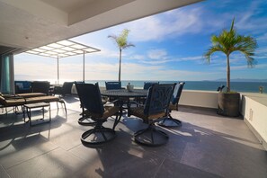 A terrace with a table and chairs, a potted palm tree, and a view of the ocean. - Caballito del Mar – 2,600 sq. ft. of Beachfront Beauty on Los Muertos Beach (Puerto Vallarta)