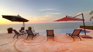 Ein Poolbereich mit Liegestühlen und Sonnenschirmen mit Blick aufs Meer.