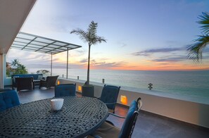 A terrace with a view of the sea at sunset, featuring a round table, chairs, and potted plants. - Caballito del Mar – 2,600 sq. ft. of Beachfront Beauty on Los Muertos Beach (Puerto Vallarta)
