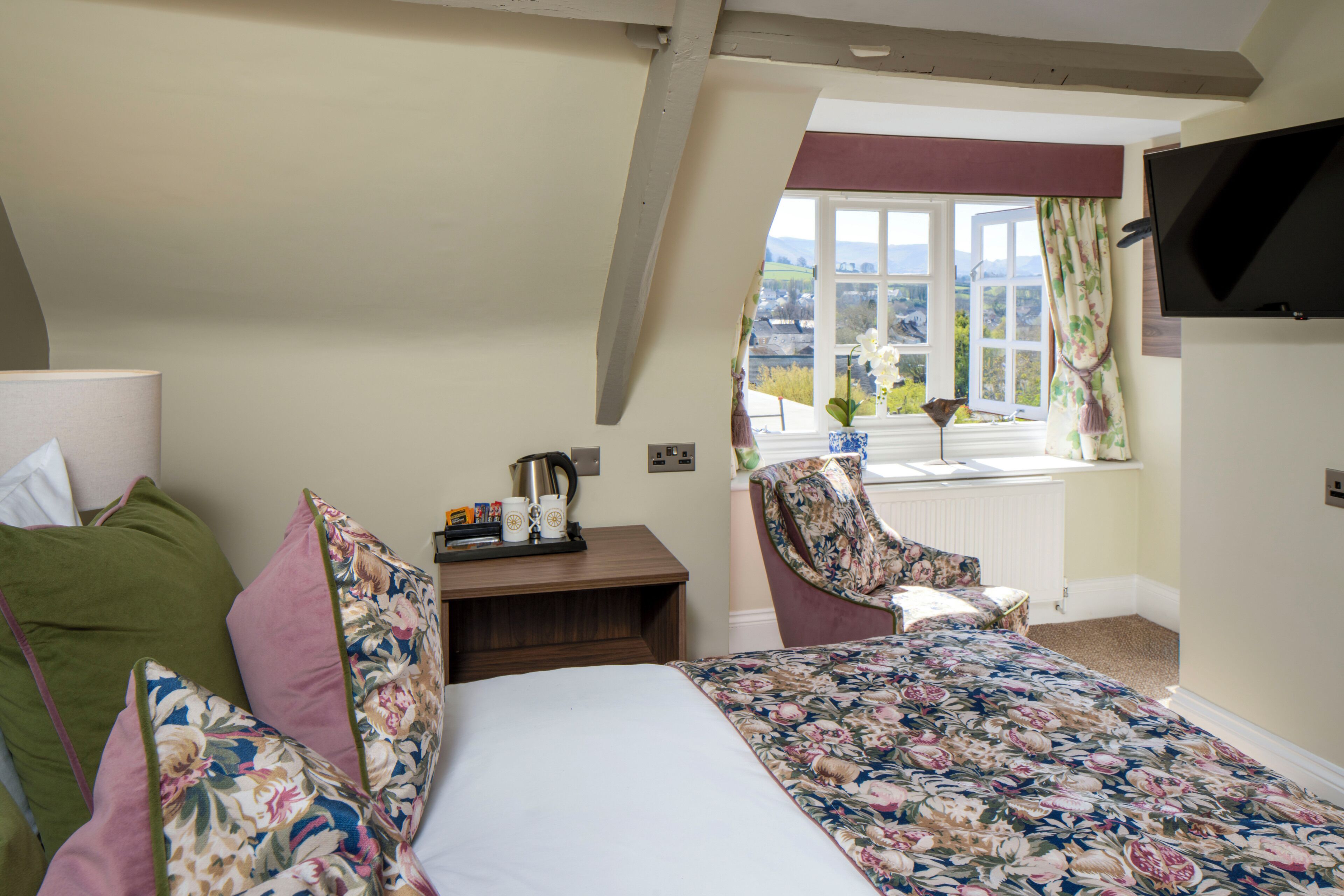 A bedroom with a bed, a chair, a table with a kettle, and a window with a view.