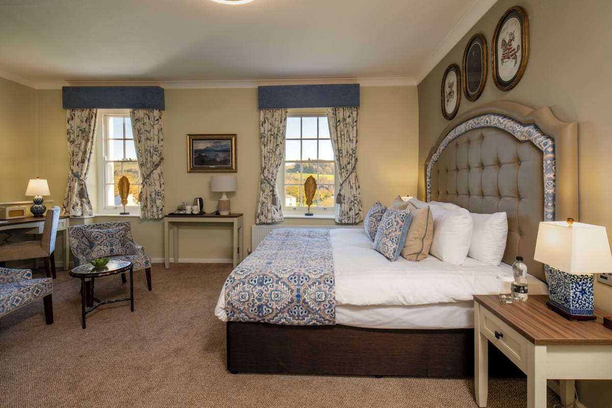 A hotel room with a bed, two chairs, a desk, a lamp, and a window with curtains.