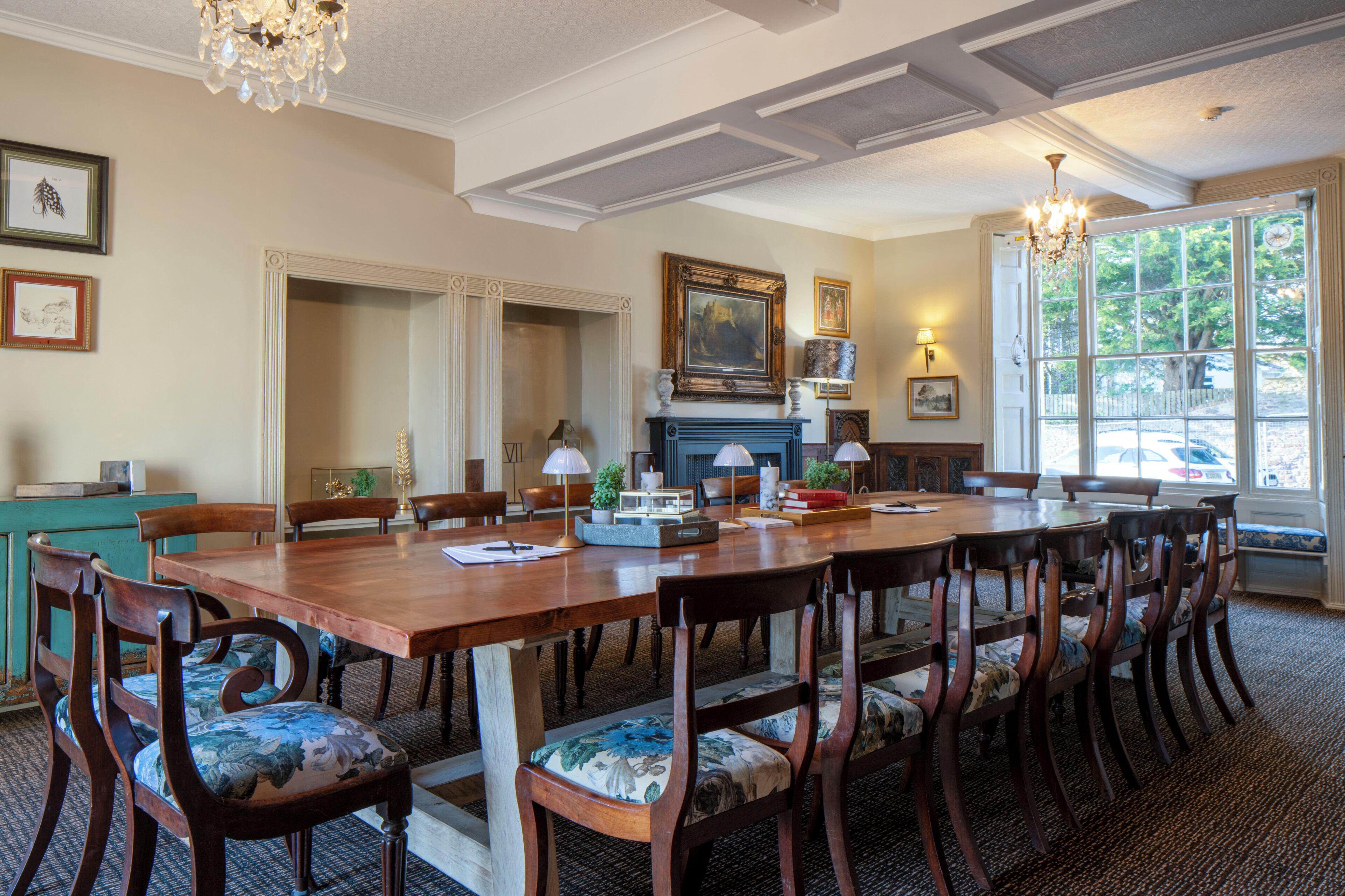 Une salle à manger élégante, avec une longue table en bois, des chaises rembourrées, une cheminée et une grande fenêtre offrant une vue panoramique.