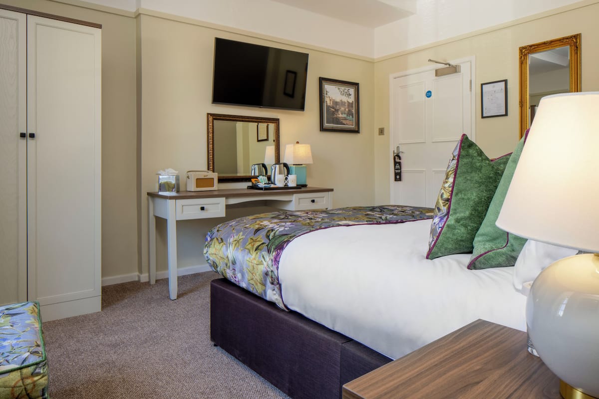 A hotel room with a bed, bedside table, lamp, dresser, mirror, and a television.