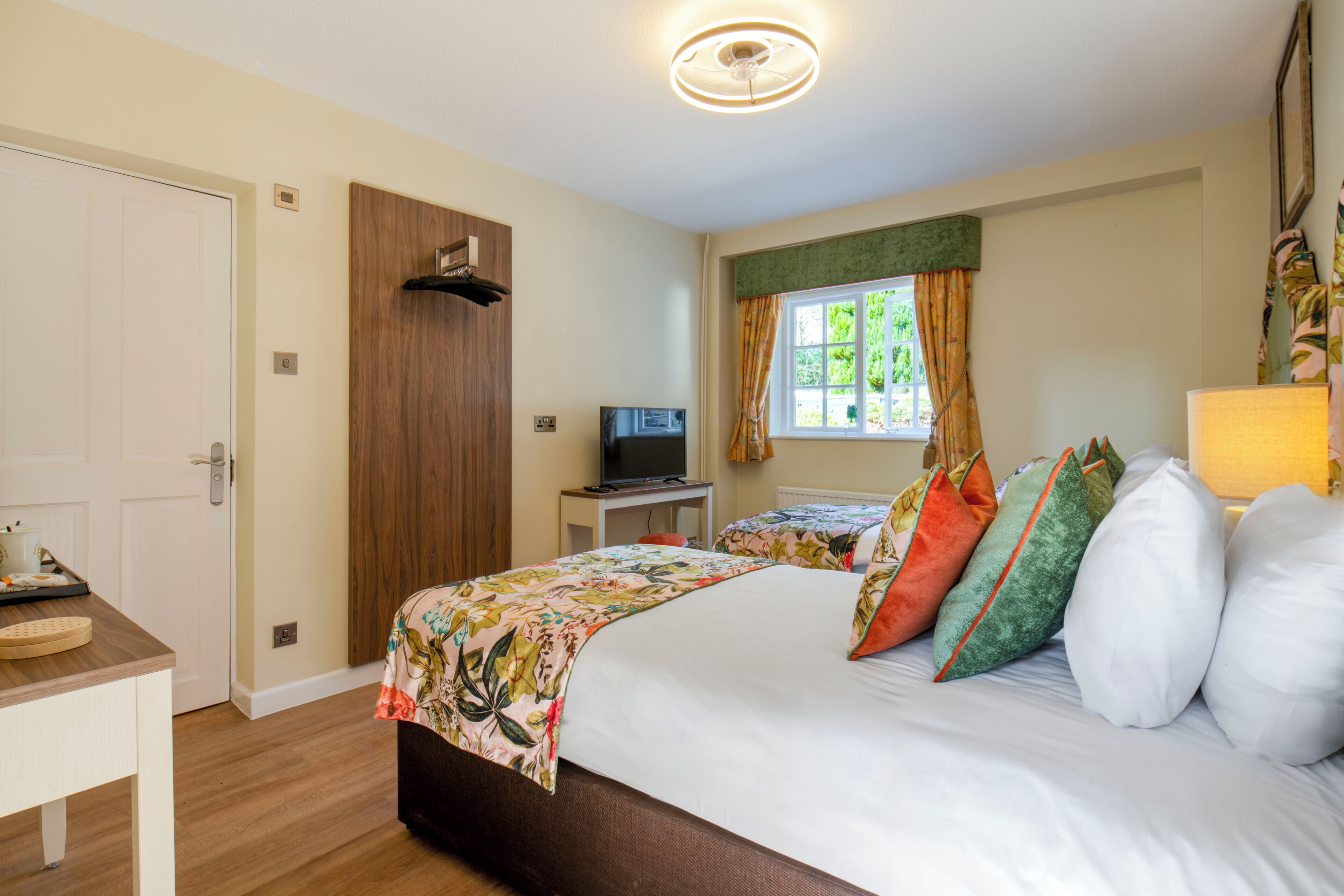 A bedroom with a bed, a television, a desk, and a window with curtains.
