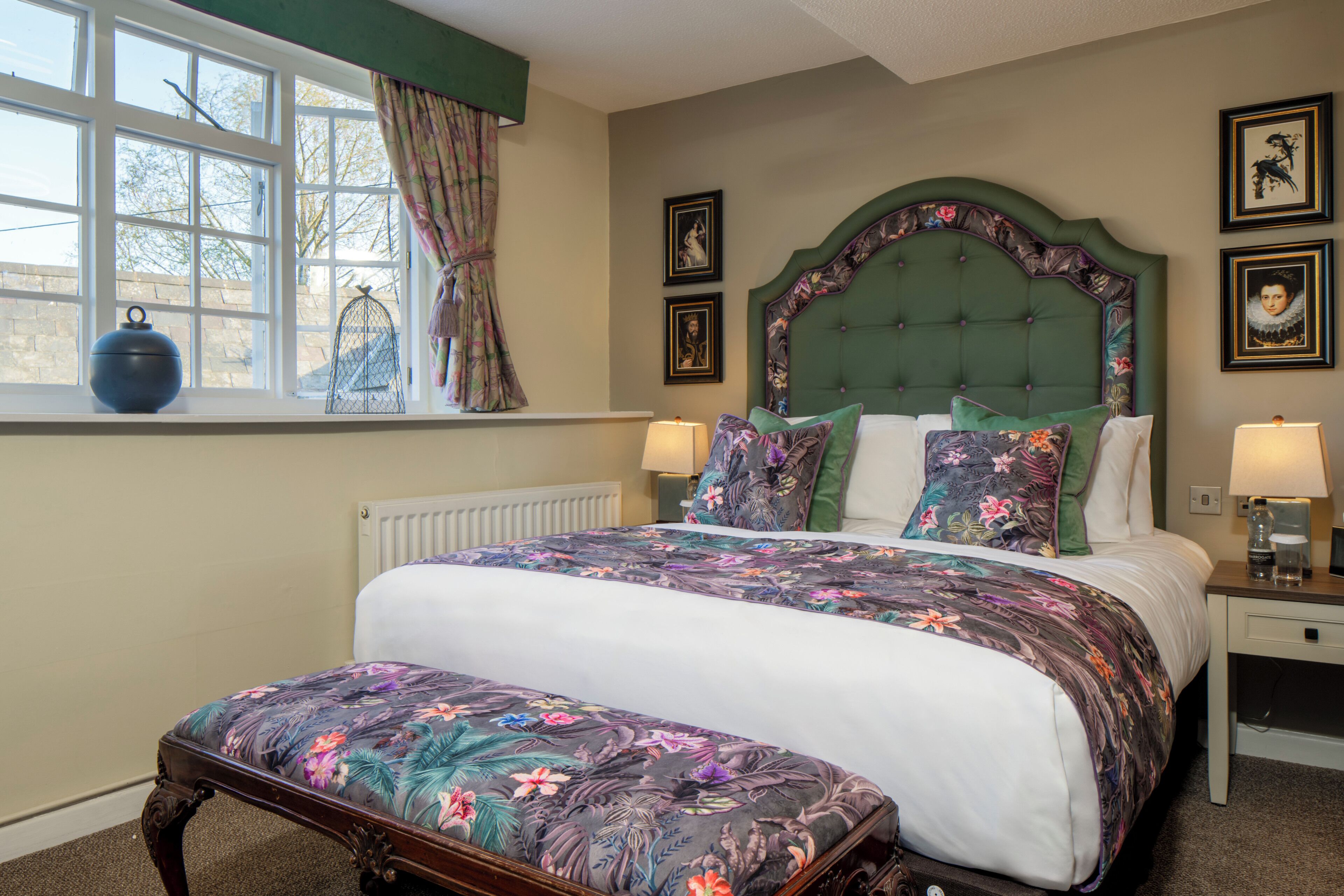 A bedroom with a large bed, a window with curtains, a radiator, and framed pictures on the wall.