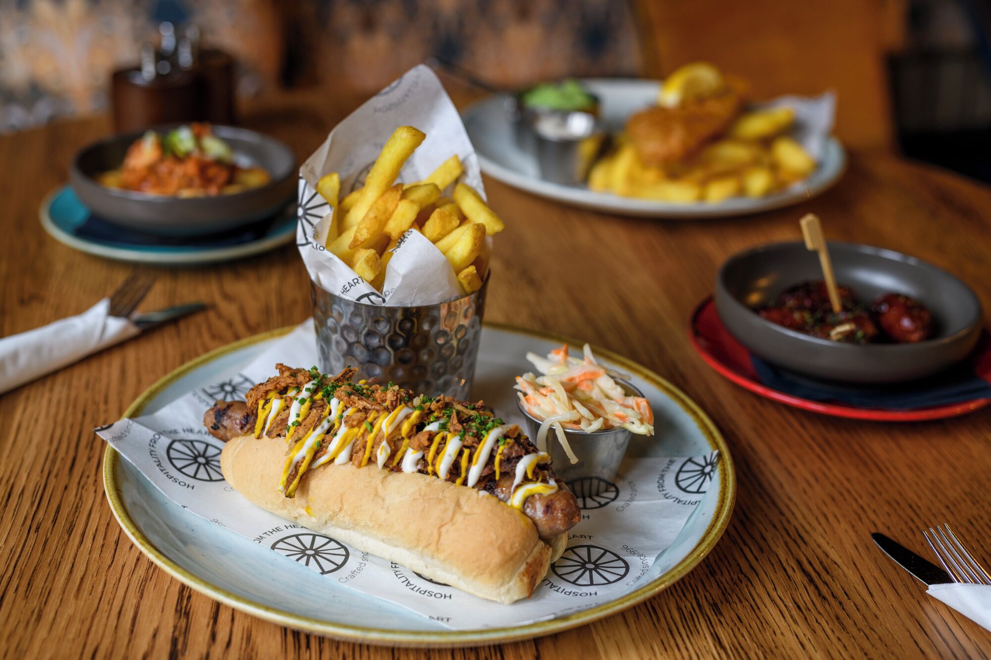 A meal with a hot dog, fries, coleslaw, and a drink on a wooden table.